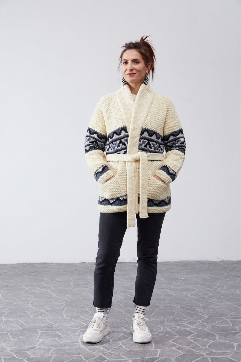Woman wearing the cream Grey Design Starsky hand-knit Cowichan-style cardigan with shawl collar and tie belt