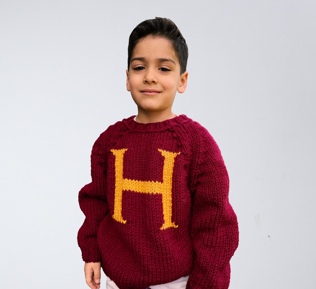 Boy wearing burgundy kids Monogram Weasley sweater with gold H letter — hand-knit wool blend