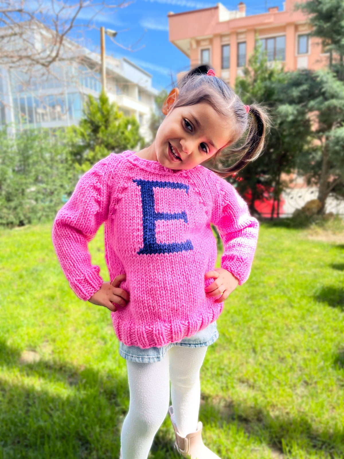 Girl in sugar pink kids monogram sweater with navy E letter — hand-knit