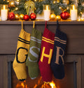 Four hand-knit monogram Christmas stockings — gold G, green S, burgundy H and navy R — hanging from a decorated mantel