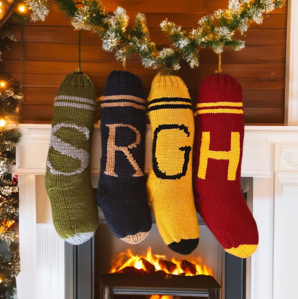 Hand-knit Weasley-style monogram stockings in green, navy, gold and burgundy hanging above a fireplace