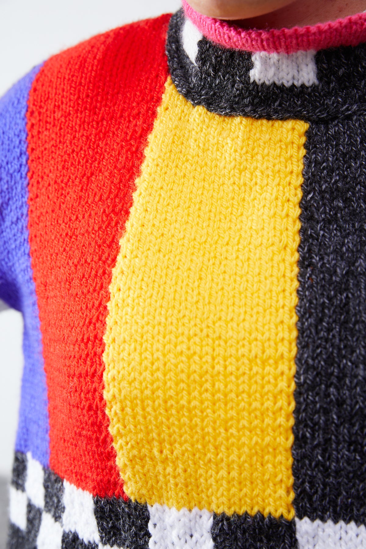 Hand-knit colorblock sweater detail: charcoal marl, red, yellow and checkerboard panels